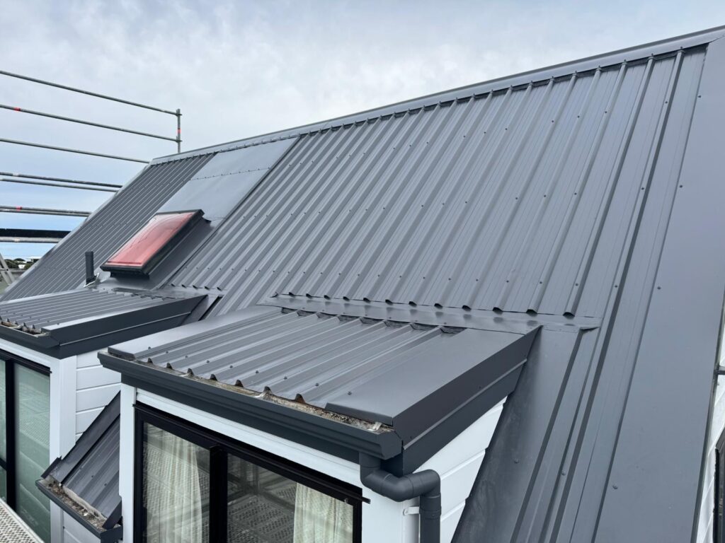 Dark metal roof with a skylight, upper roof plane and several lower roof-to-wall junctions