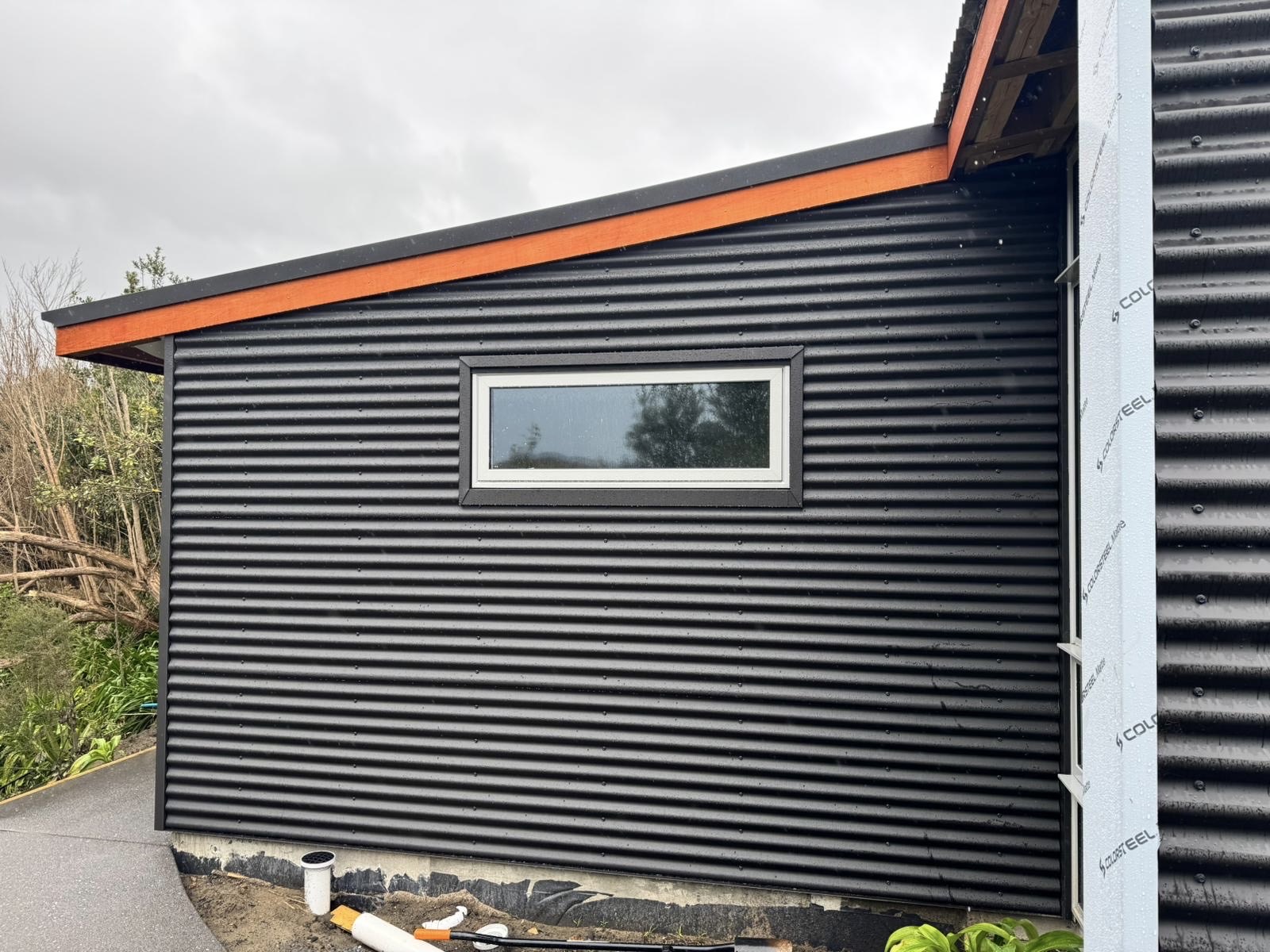 Dark horizontal corrugated metal wall cladding fitted around a rectangular window opening