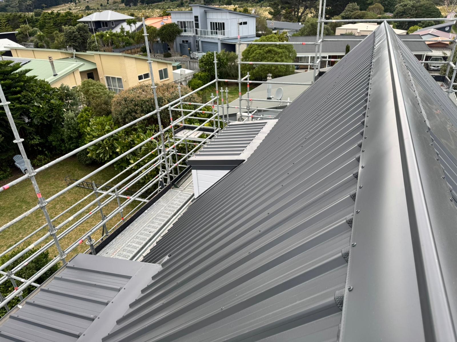 Dark long-run metal roof with ridge capping and scaffolding on a Wellington property